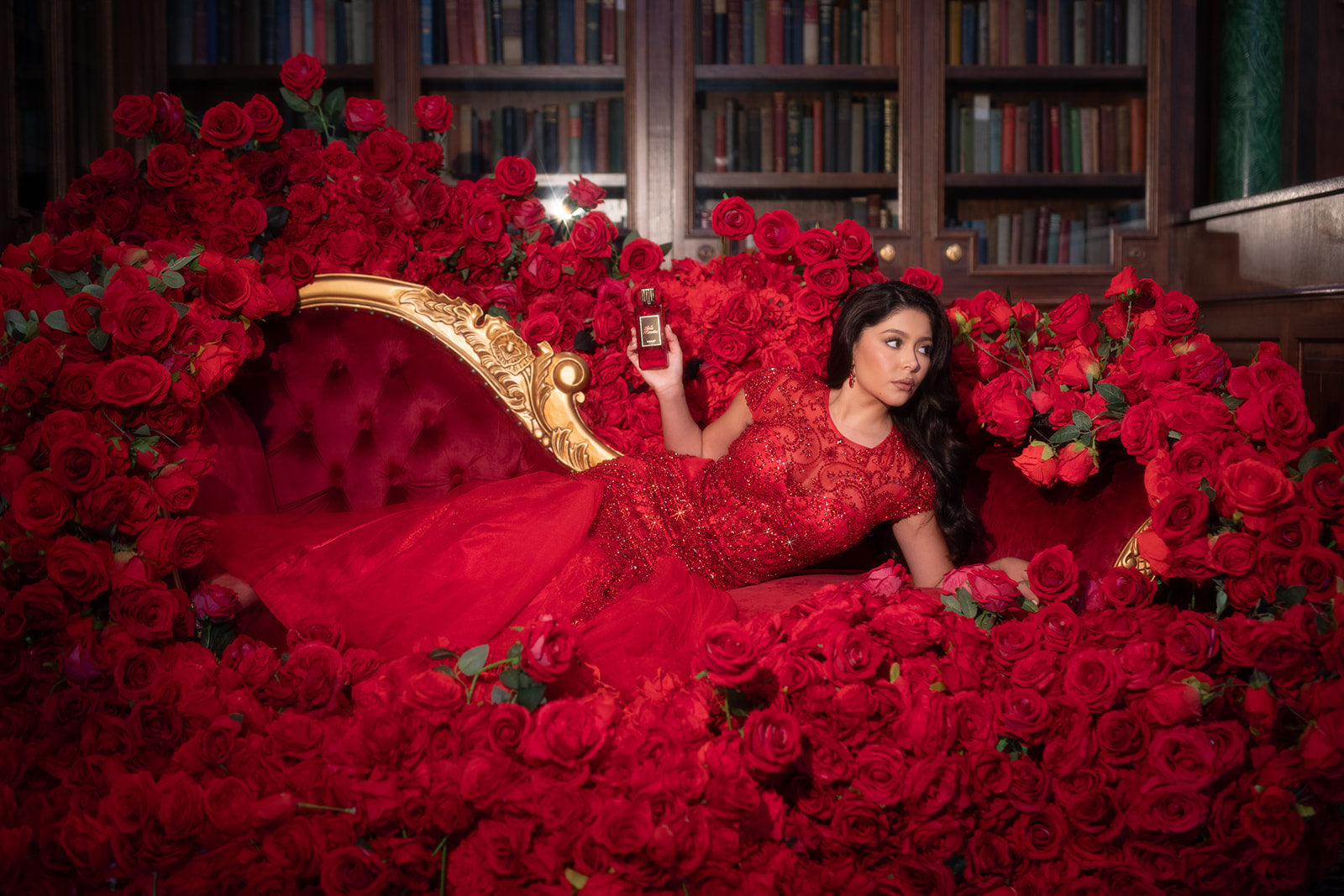 Daisy Marquez lounging on a velvet couch, surrounded by roses, as she poses with her signature fragrance, Scarlet.